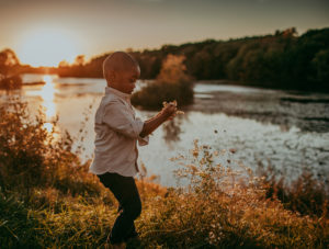 Family Photographer, a young boy lifts flowers from ground near a quiet river